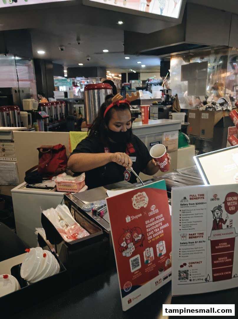 An employee at LiHO TEA prepares a bubble tea drink behind the counter.