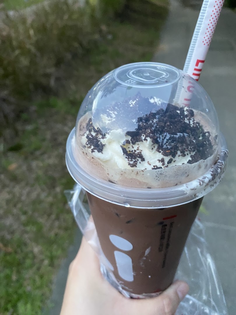 A hand holds a chocolate drink from LiHO TEA, topped with whipped cream and cookie crumbs.