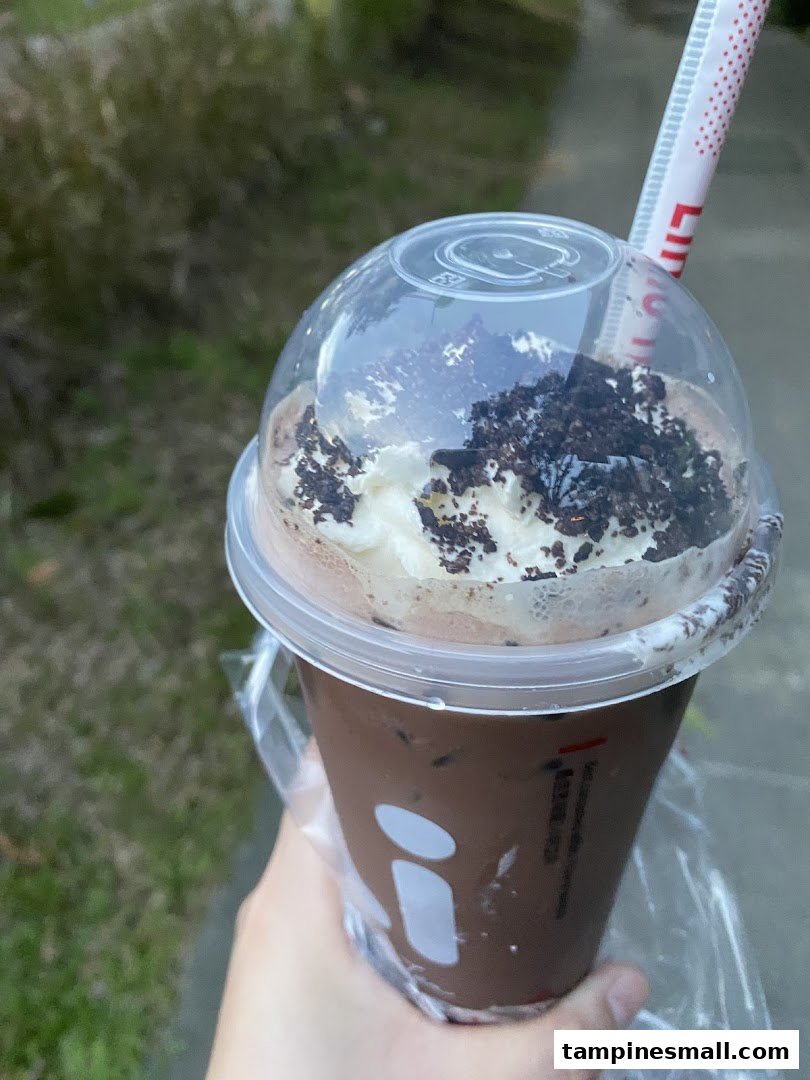 A hand holds a chocolate drink from LiHO TEA, topped with whipped cream and cookie crumbs.