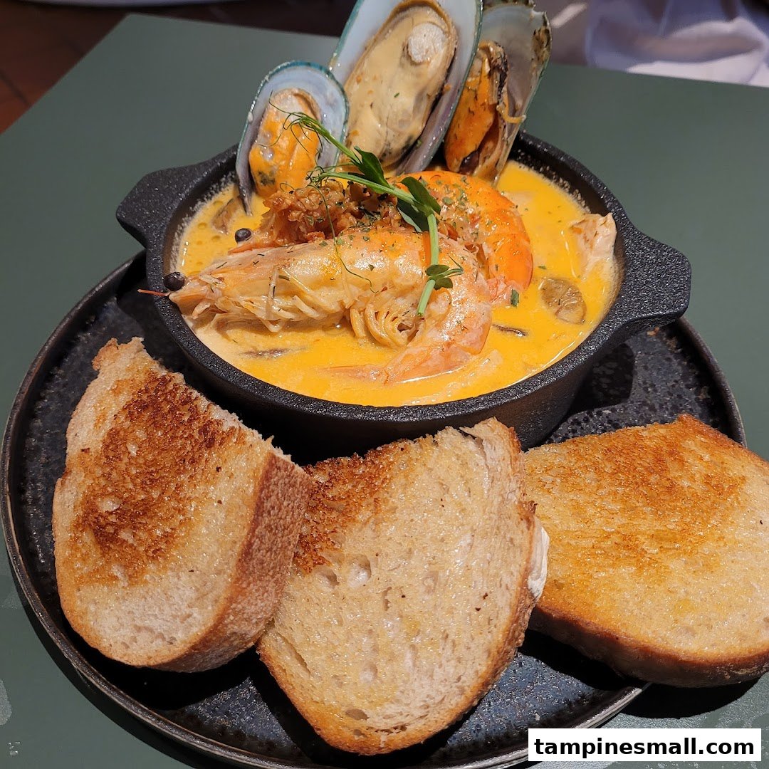 A vibrant seafood dish featuring prawns, mussels, and a creamy sauce, served with toasted bread.