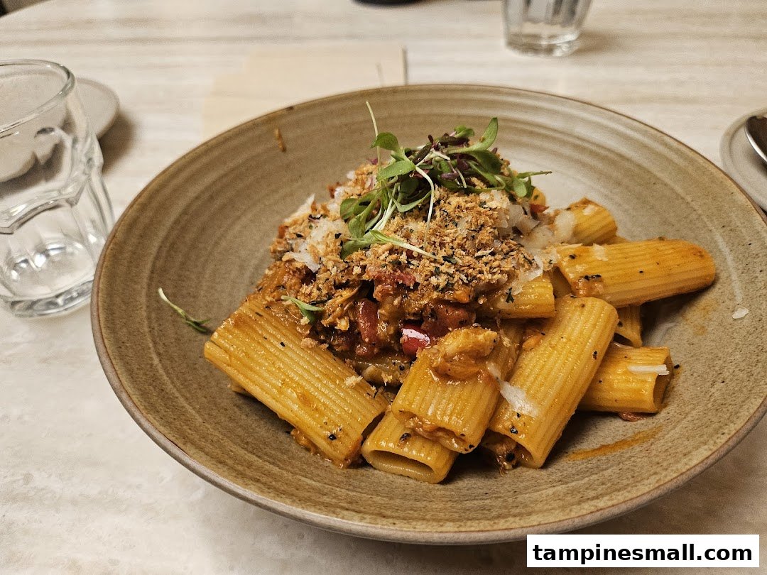 A close-up of a delicious pasta dish with rigatoni, rich sauce, breadcrumbs, and fresh greens.
