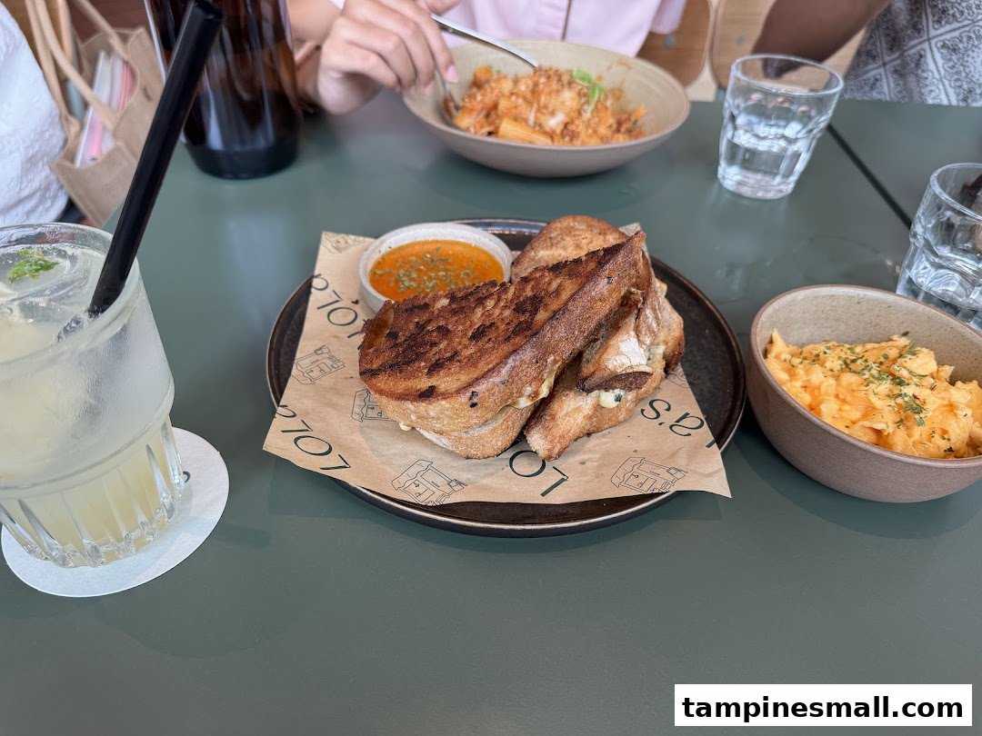 A delicious meal featuring a grilled cheese sandwich, scrambled eggs, pasta, and a refreshing drink on a green table.