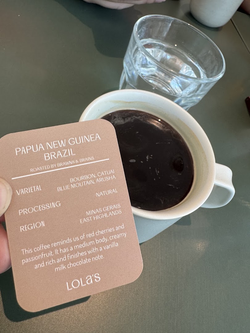 A hand holds a coffee information card next to a cup of coffee and a glass of water.