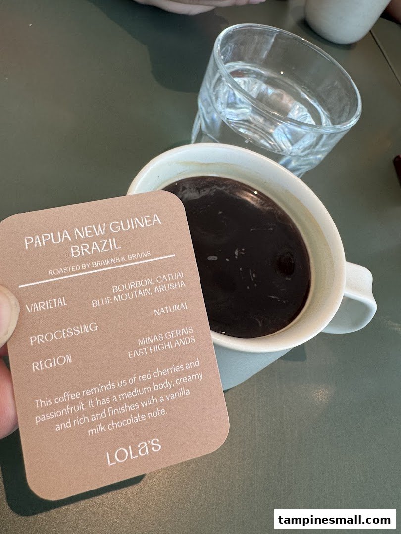 A hand holds a coffee information card next to a cup of coffee and a glass of water.