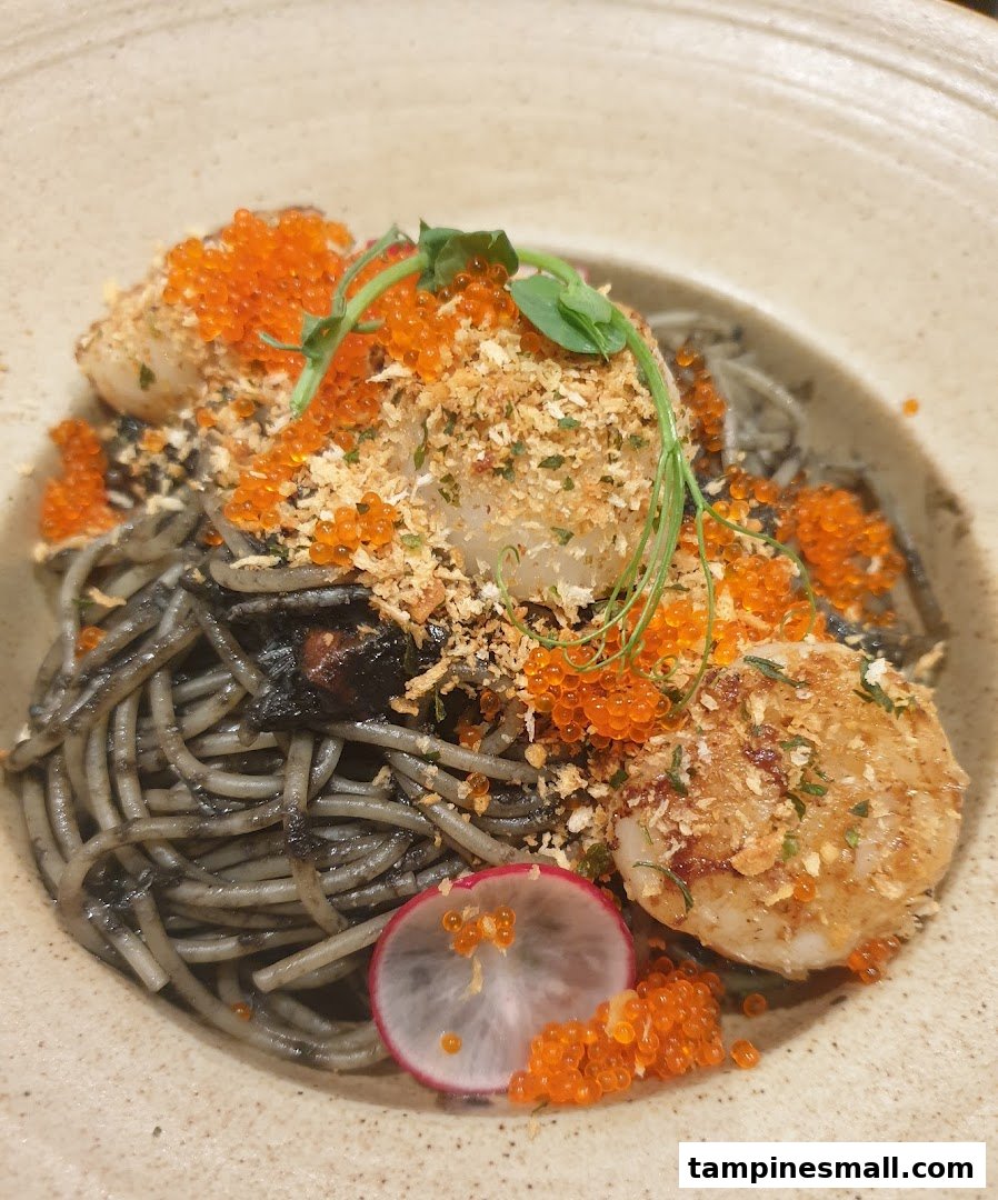 A gourmet dish featuring black pasta with seared scallops, vibrant orange roe, and a radish garnish.