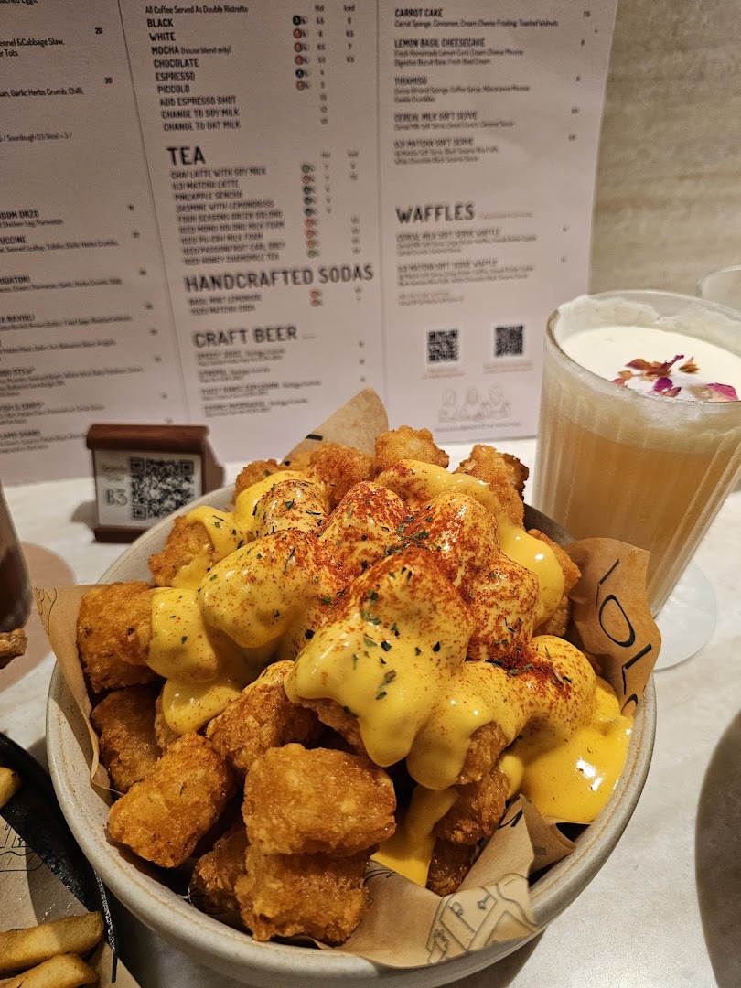 A bowl of cheesy tater tots and a drink, with a detailed menu visible in the background.
