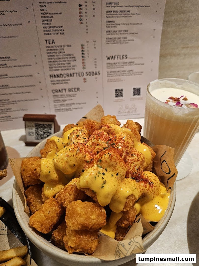 A bowl of cheesy tater tots and a drink, with a detailed menu visible in the background.