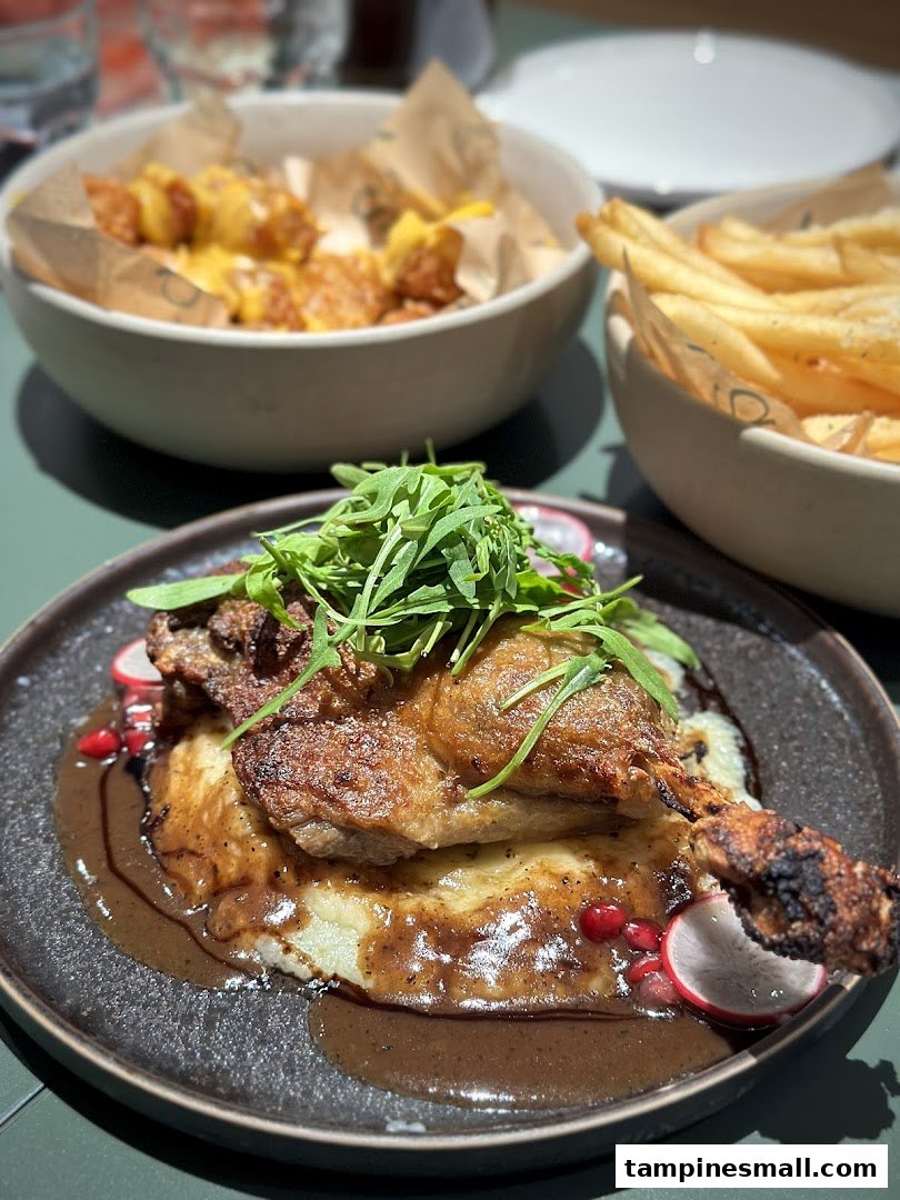 A delicious roasted duck leg with mashed potatoes and gravy, served with sides of fries and cheesy potato bites.