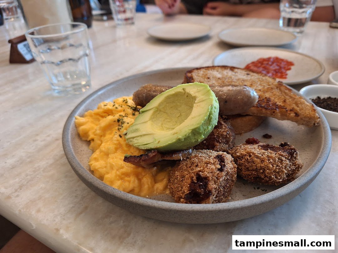 A delicious breakfast plate featuring scrambled eggs, avocado, sausage, toast, and crispy croquettes at Lolas.