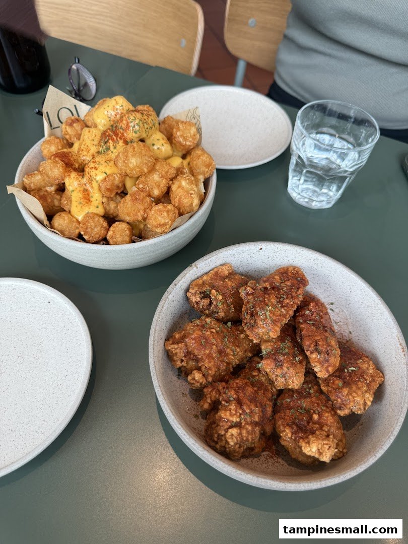 A table featuring two bowls of food: cheesy tater tots and crispy chicken wings.