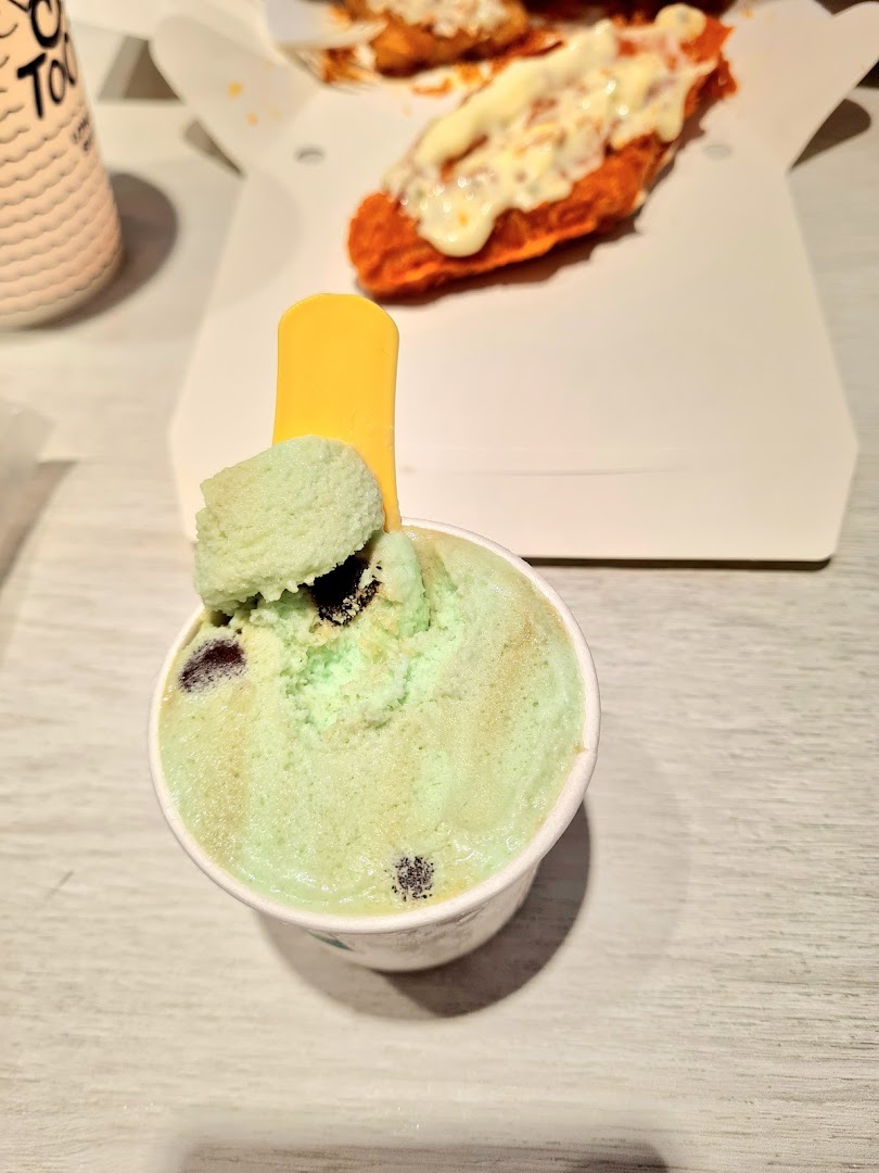 A refreshing cup of mint chocolate chip ice cream with a yellow spoon, alongside a box of savory fried food.
