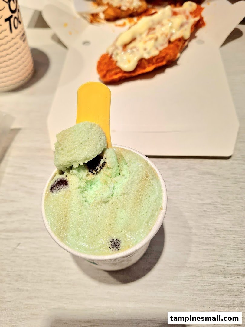 A refreshing cup of mint chocolate chip ice cream with a yellow spoon, alongside a box of savory fried food.