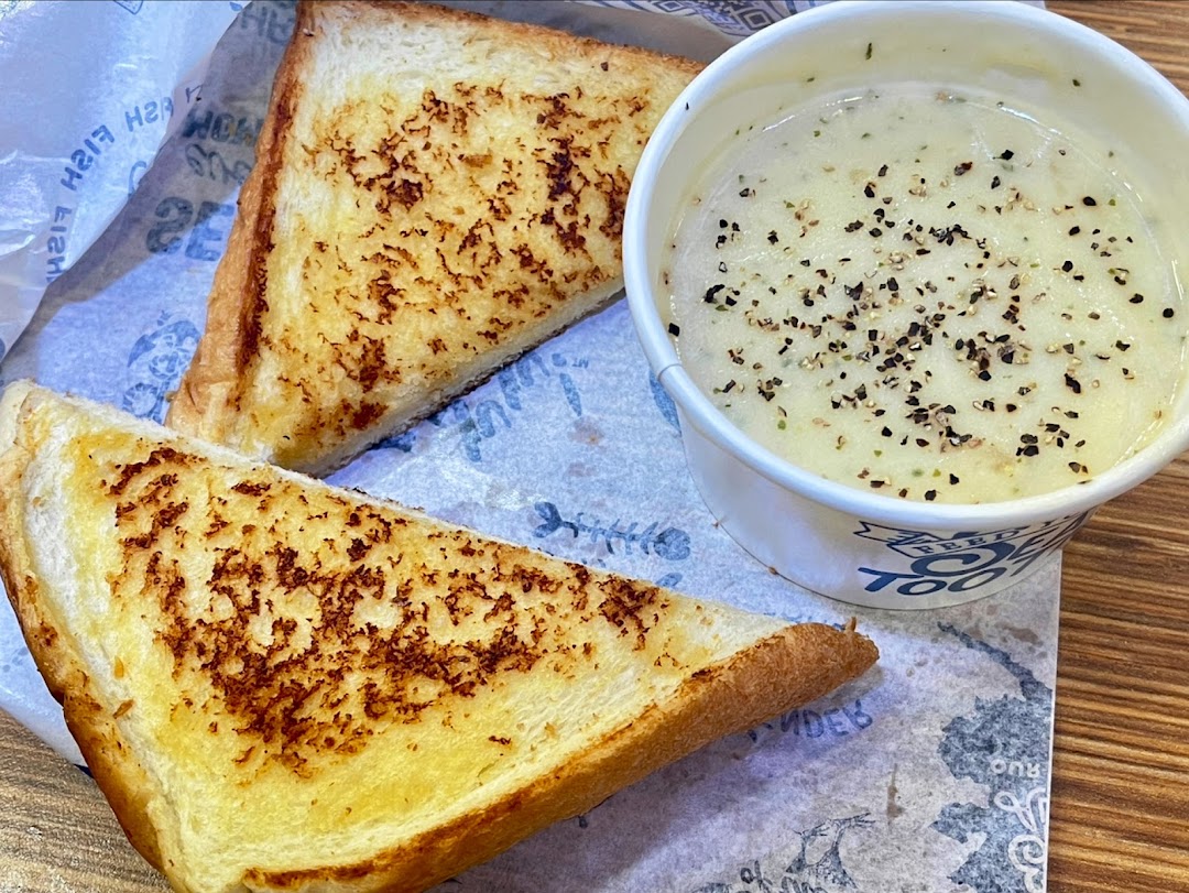 A close-up of two grilled toast slices and a cup of creamy soup with black pepper.