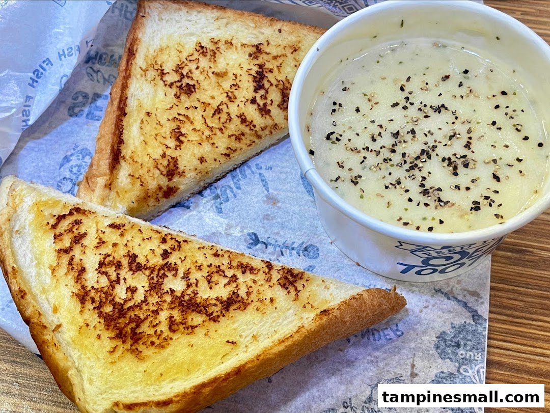 A close-up of two grilled toast slices and a cup of creamy soup with black pepper.