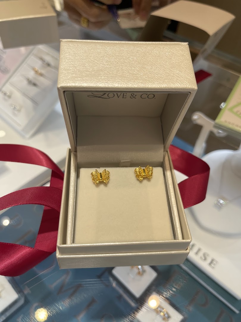 A pair of golden bow-shaped earrings displayed in an open Love & Co. gift box with a red ribbon.