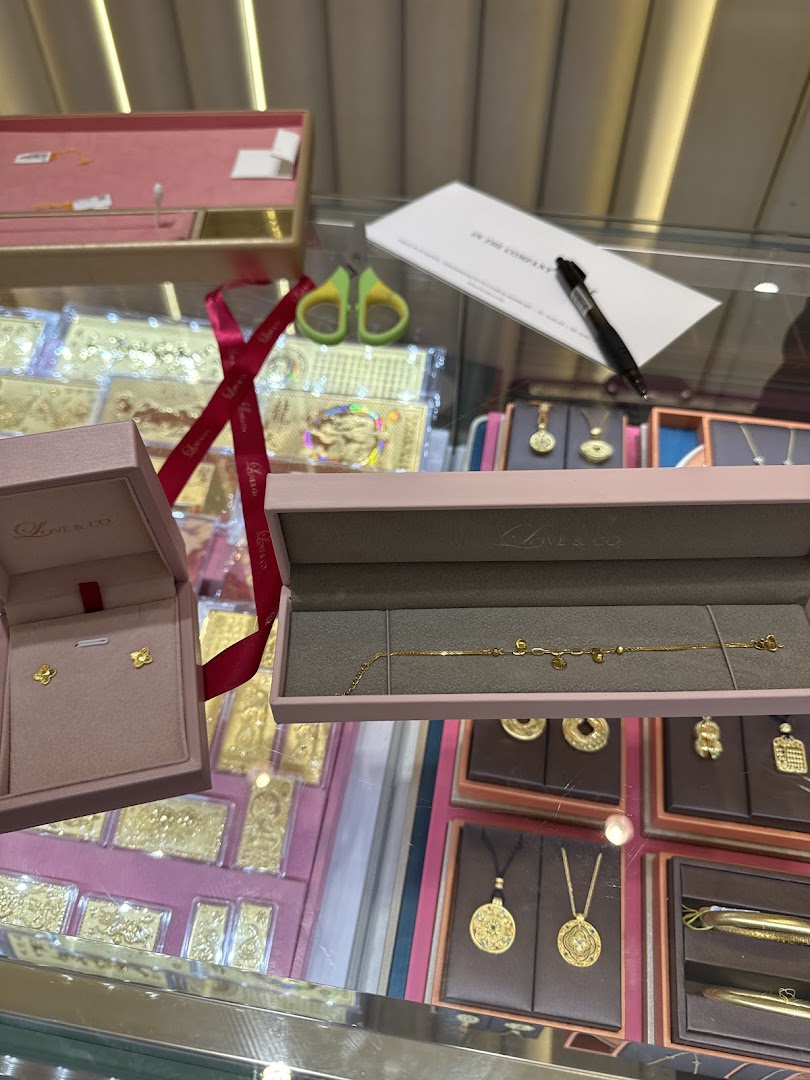 Close-up of exquisite gold jewelry, including earrings and a bracelet, displayed in pink boxes within a retail setting.