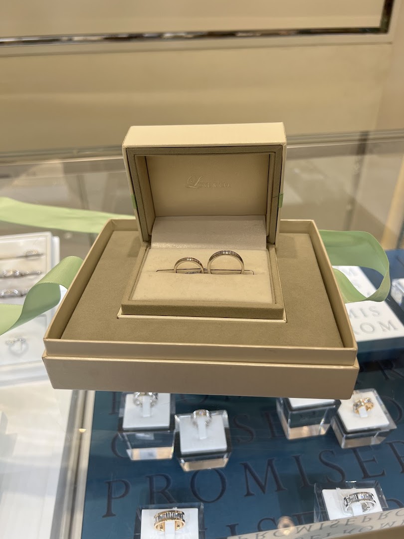 A pair of elegant wedding bands displayed in a Love & Co. ring box, surrounded by other rings.