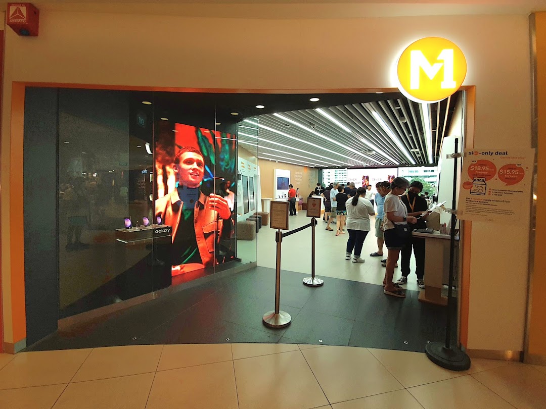 The entrance of M1 Tampines Mall, a phone and internet service shop, with a large digital display and customers inside.