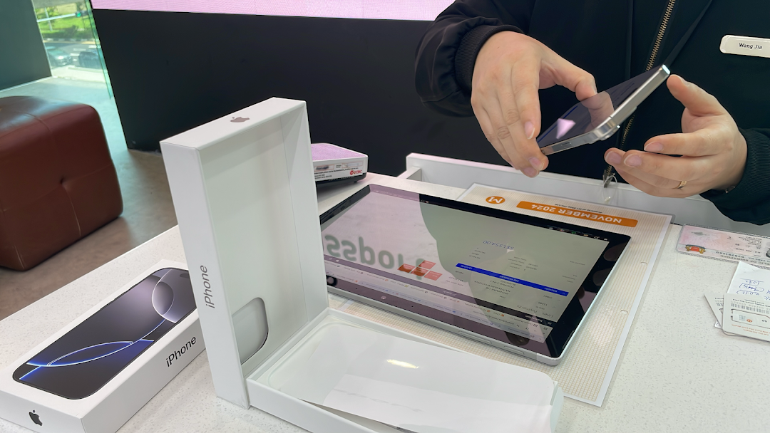 A staff member assists a customer with a new iPhone, showcasing the device and its packaging.