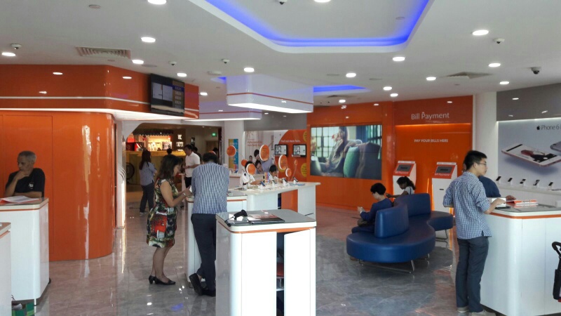 Customers browse phones and interact with staff in a modern, orange-themed phone and internet service shop.