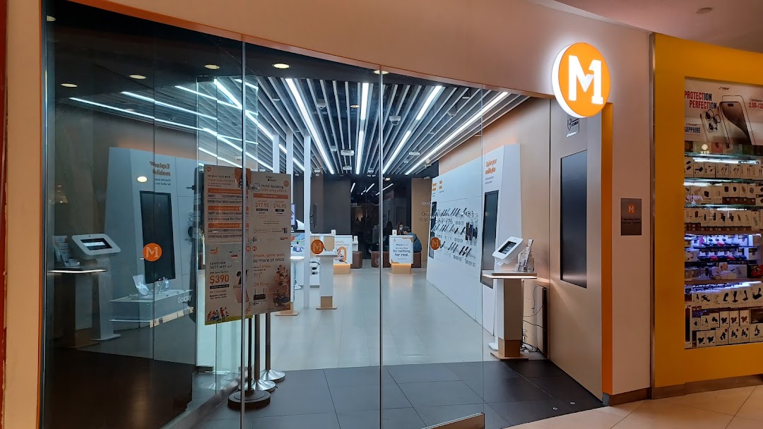 The brightly lit entrance of M1, a phone and internet service provider shop, is visible.