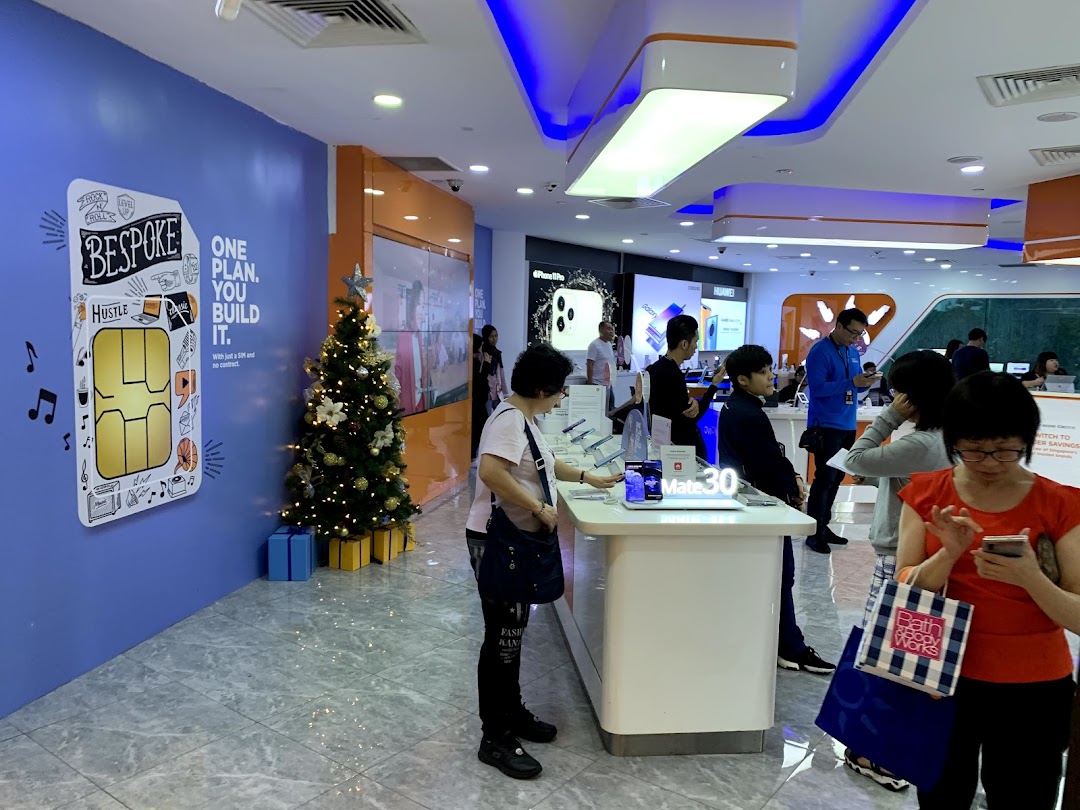 Customers browse smartphones and internet services in a modern, brightly lit M1 store with festive decorations.