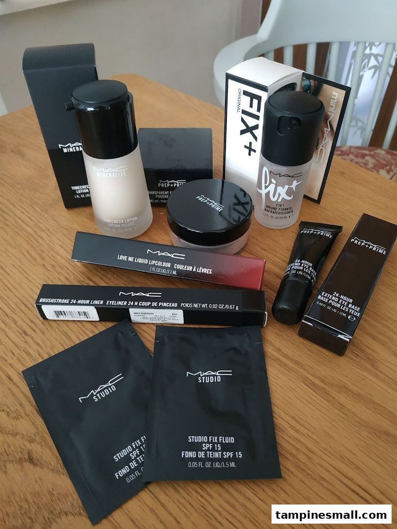 A collection of MAC Cosmetics makeup products, including foundations, primers, and samples, on a wooden table.