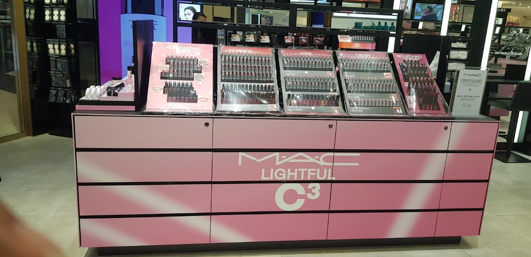 A pink MAC Cosmetics display counter showcasing various lip products in a retail store.