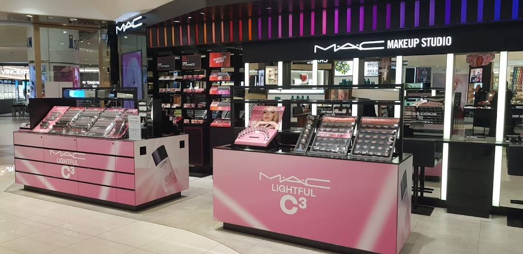 An interior view of MAC Cosmetics, showcasing makeup displays and product counters with pink branding.