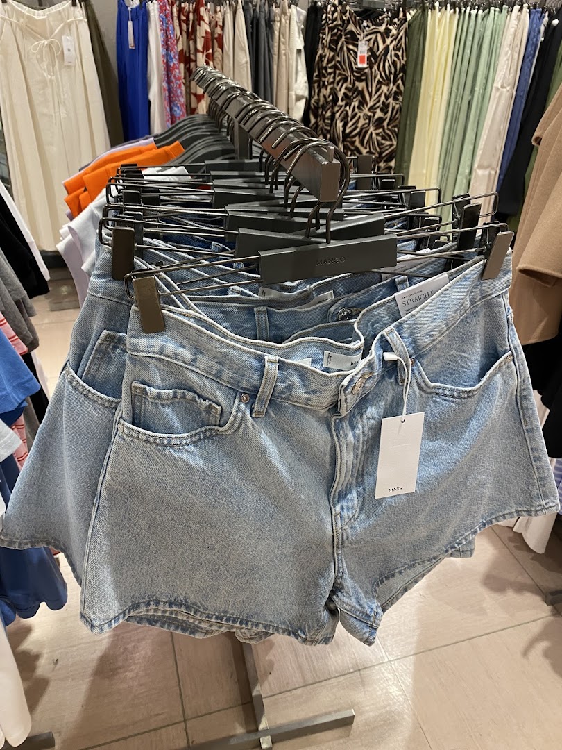 Light blue denim shorts displayed on a rack inside a Mango clothing store, surrounded by other apparel.