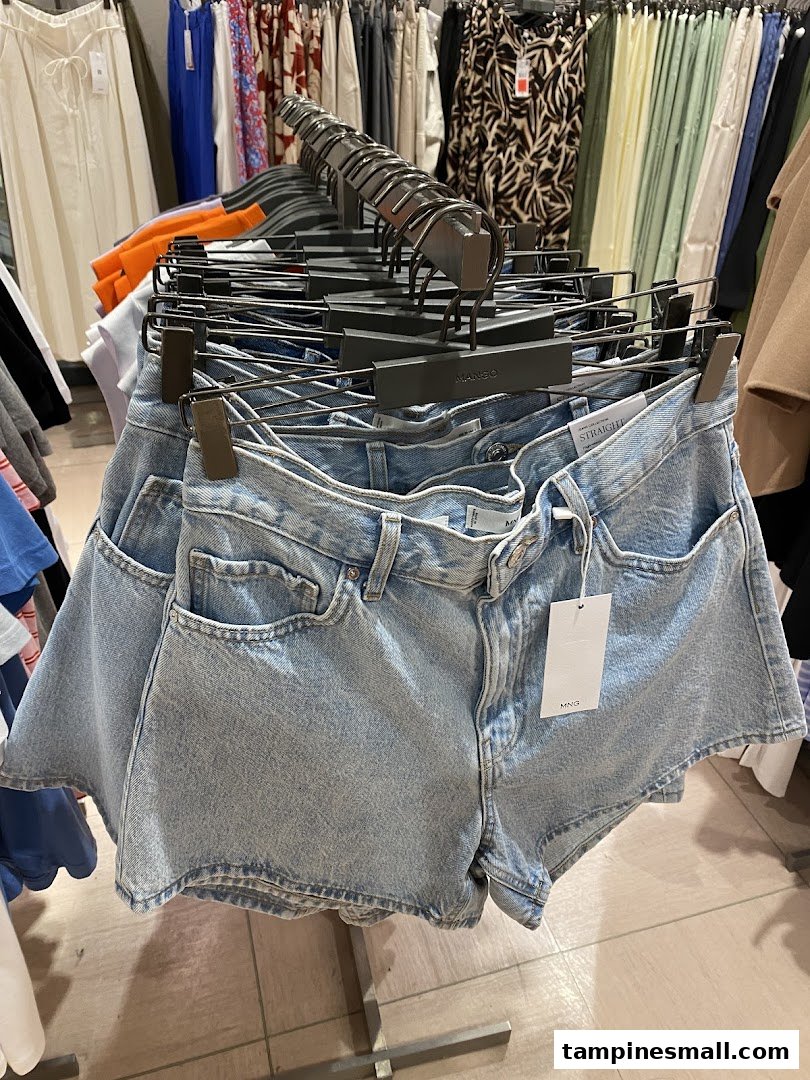 Light blue denim shorts displayed on a rack inside a Mango clothing store, surrounded by other apparel.