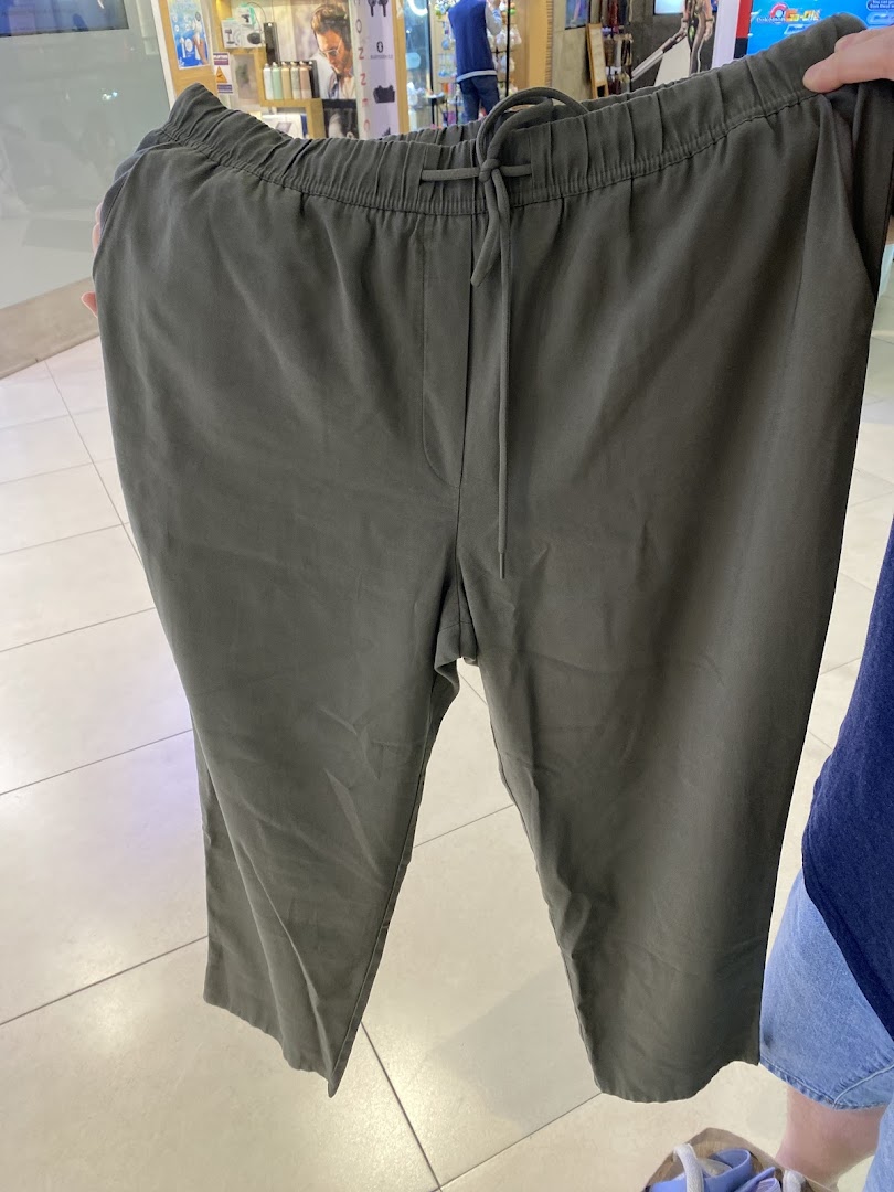 A person holds up a pair of comfortable dark green casual trousers with a drawstring waist.