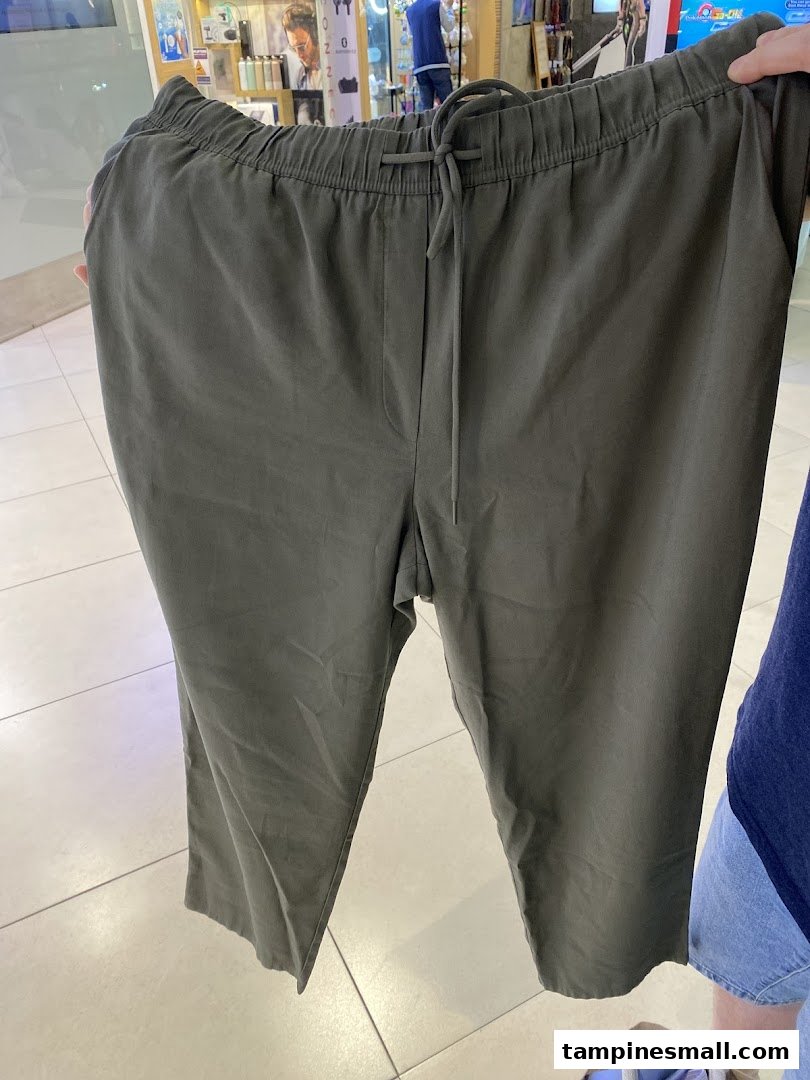 A person holds up a pair of comfortable dark green casual trousers with a drawstring waist.
