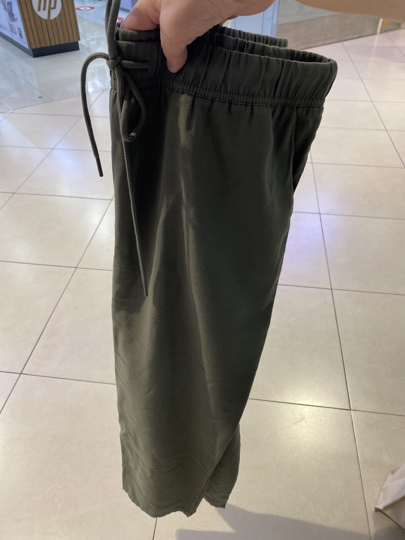 A person holds a pair of olive green elastic-waist pants inside a retail store.