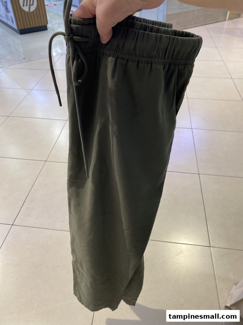 A person holds a pair of olive green elastic-waist pants inside a retail store.
