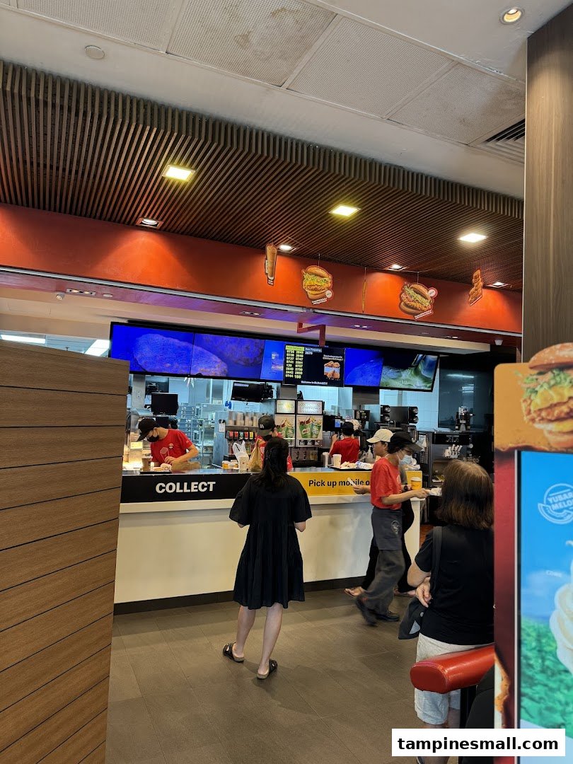 Interior view of McDonald's showing the service counter, staff, and customers waiting to collect orders.