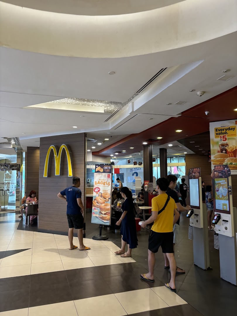 Customers gather near the entrance of McDonald's, featuring self-service kiosks and promotional signage.