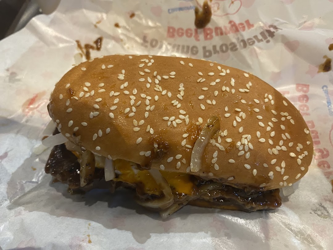 A close-up shot of a delicious-looking burger with sesame seeds, onions, and sauce on a wrapper.
