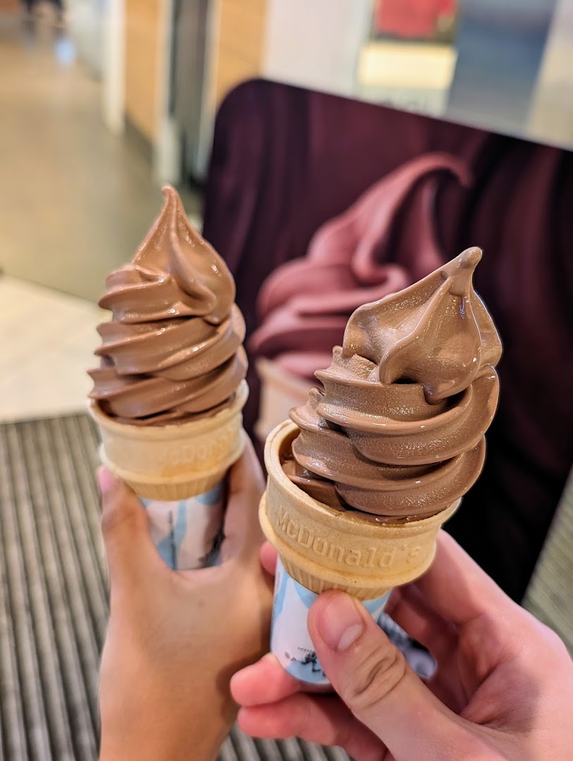 Two hands hold delicious chocolate soft-serve ice cream cones from McDonald's.