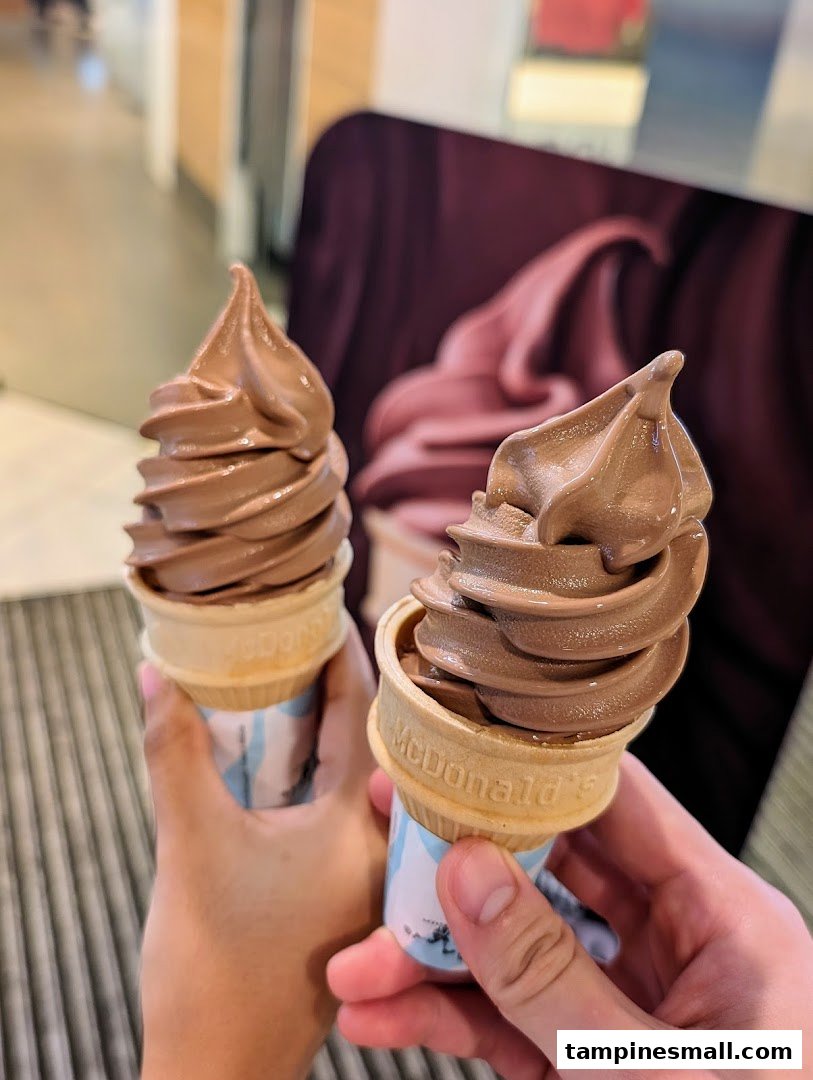 Two hands hold delicious chocolate soft-serve ice cream cones from McDonald's.