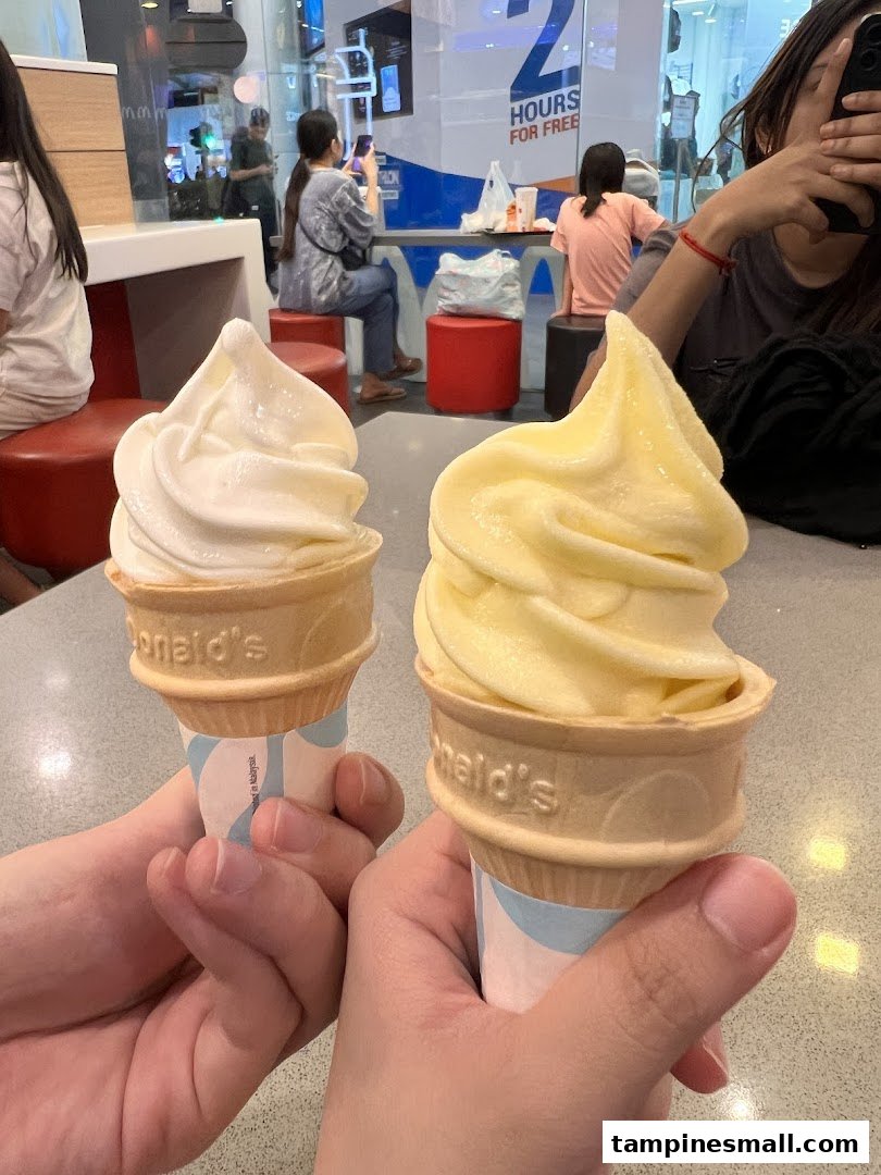 Two hands hold vanilla and pineapple soft-serve ice cream cones inside a McDonald's restaurant.