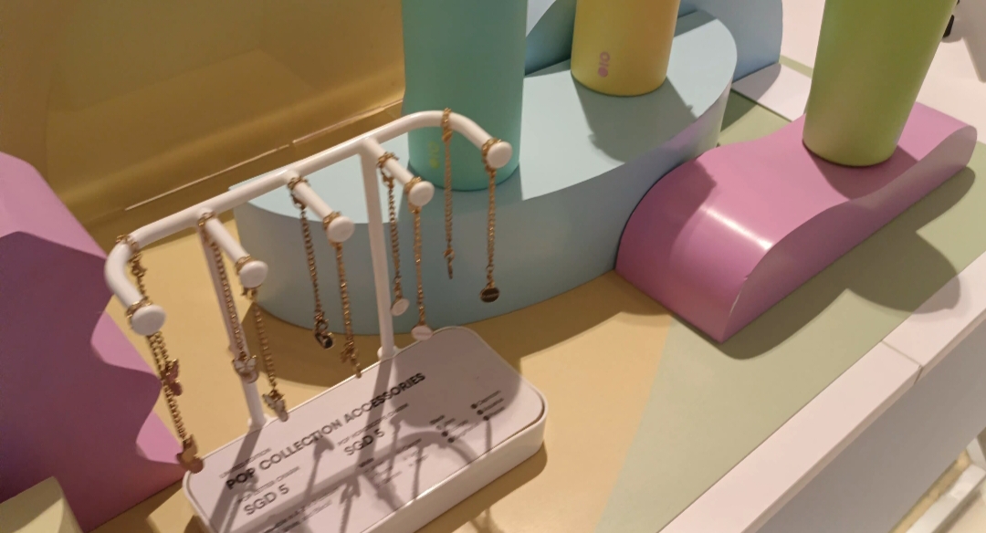 A vibrant retail display featuring gold-colored charms on a stand and colorful bottles, set against pastel props.