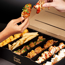 Hands pick up delicious chicken wings from a variety snack box with fries and potato bites.