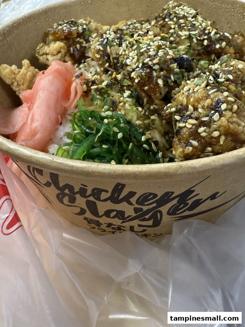 A close-up of a delicious rice bowl with crispy fried chicken, seaweed, and pickled ginger.
