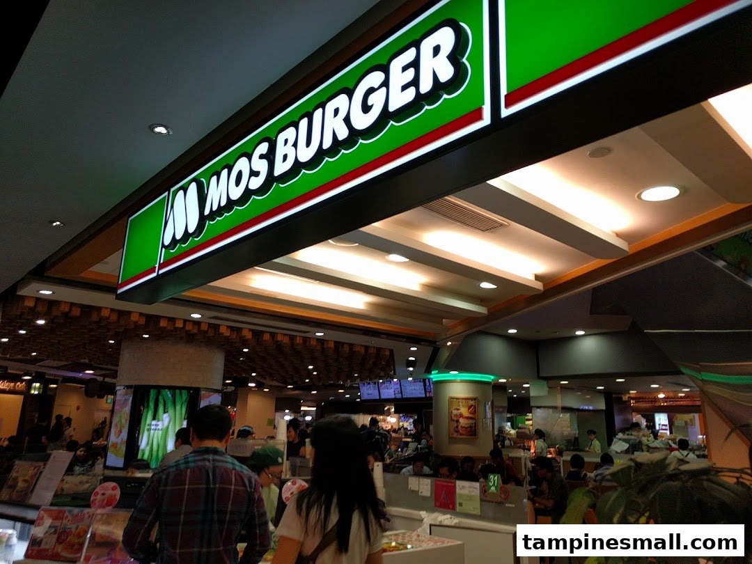 An illuminated MOS Burger sign hangs above a bustling food court area with customers.