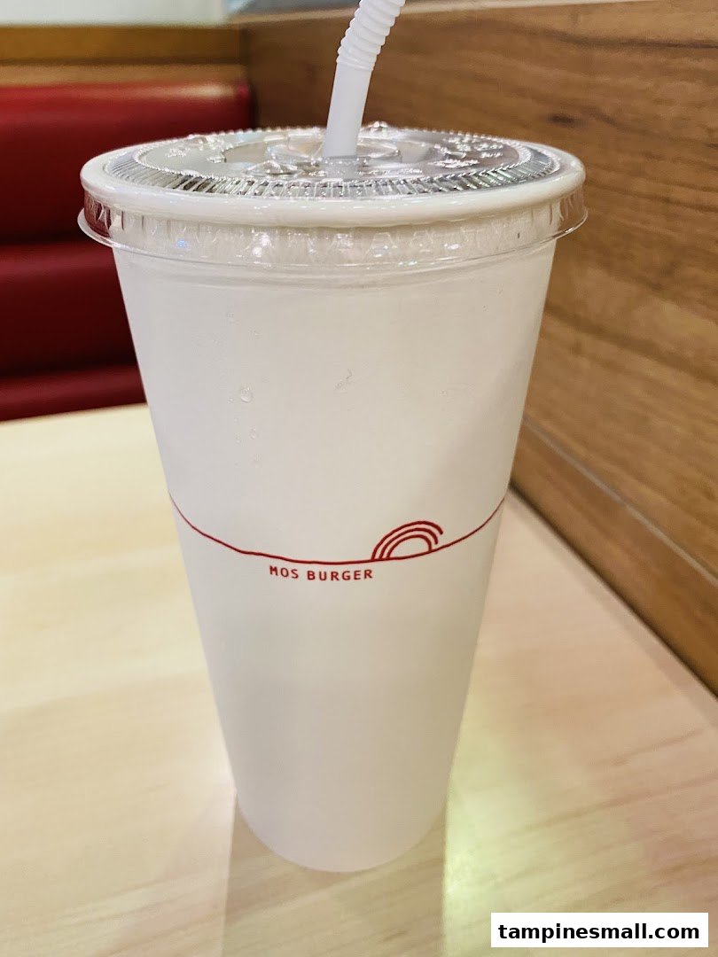 A white drink cup with a straw and the MOS Burger logo on a light wooden table.