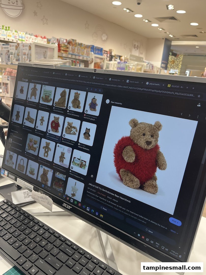 An employee's computer screen displaying Jellycat bears, with baby products and shop interior visible in the background.