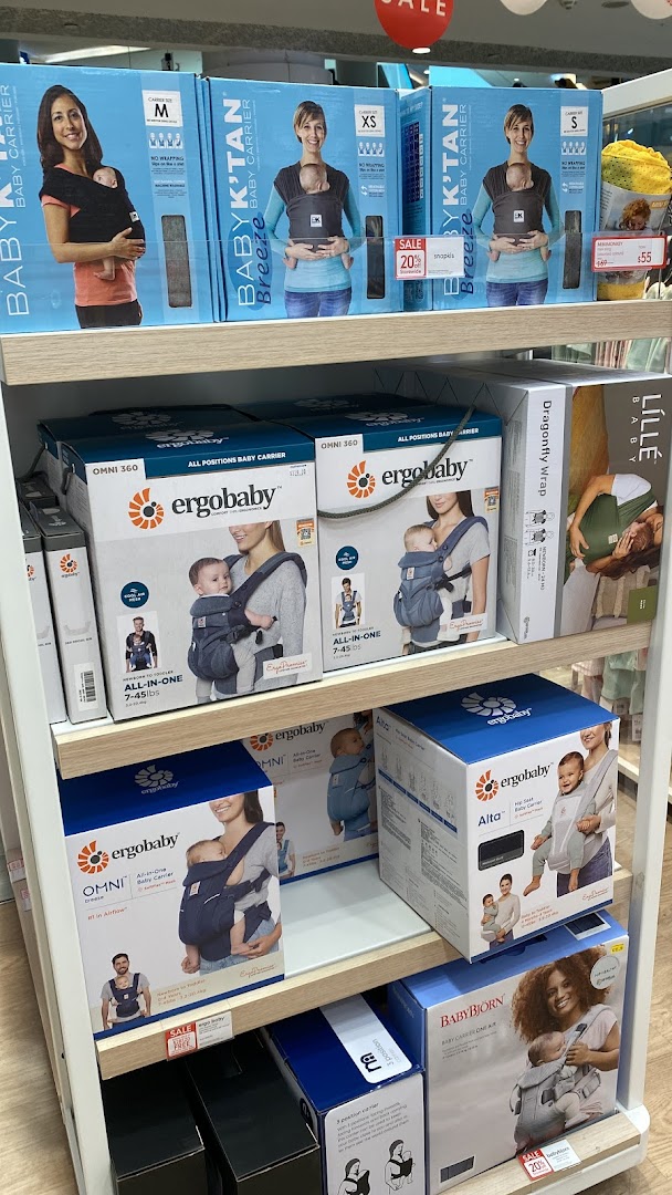 A retail display shelf at Mothercare showcasing various baby carriers and accessories.