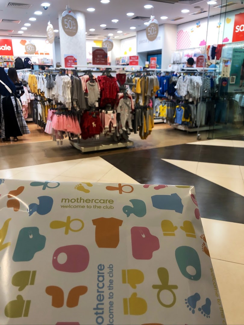 Interior view of Mothercare, featuring baby clothing racks, sale signs, and a branded shopping bag.