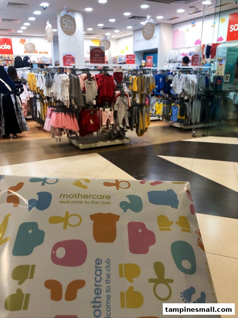 Interior view of Mothercare, featuring baby clothing racks, sale signs, and a branded shopping bag.
